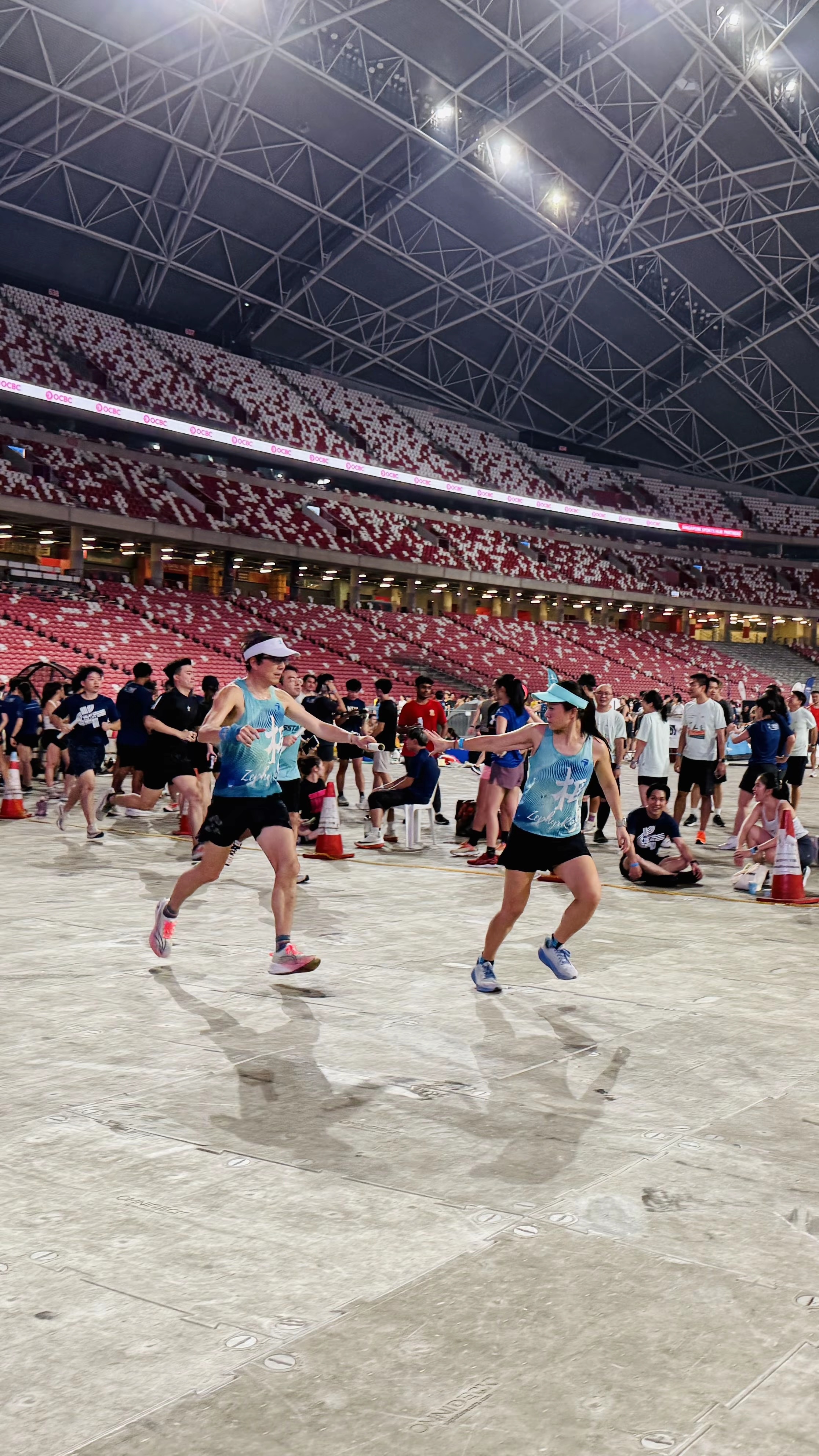 Zephyr runners passing the baton inside Singapore National Stadium at night